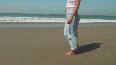 young woman walking on the beach in jeans and makes footsteps in the sand