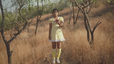 Young-beautiful-girl-holding-a-clay-pot-outdoors-in-the-fields-with-prominent-trees-surrounding-them