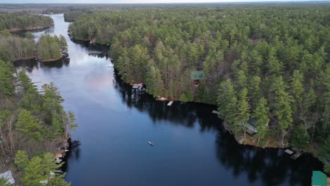 aerial view of a person canoeing on a calm forest river, surrounded by dense trees and cabins along the banks