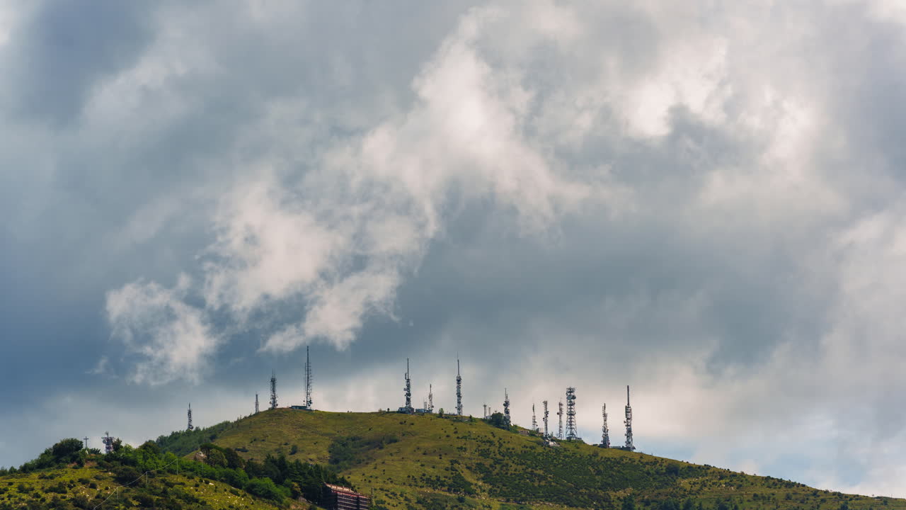 Fast-moving clouds over hilltop covered with communication antennas and towers, stormy weather sky