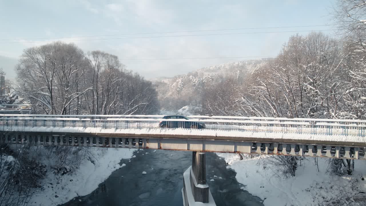 눈, 얼어붙은 강, 눈 덮인 숲으로 덮인 다리를 건너는 자동차의 공중 전망