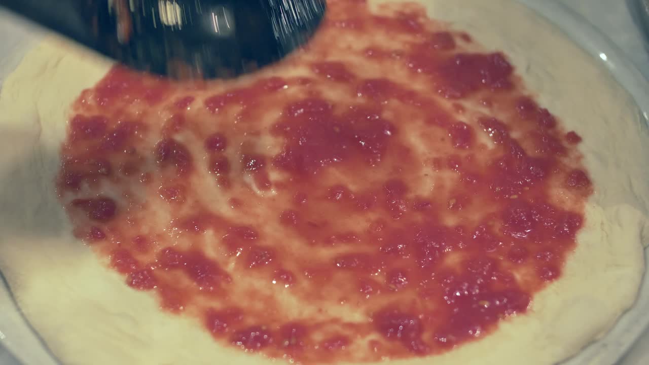 chef italiano esparciendo en círculos salsa de tomate fresco sobre la masa de pizza