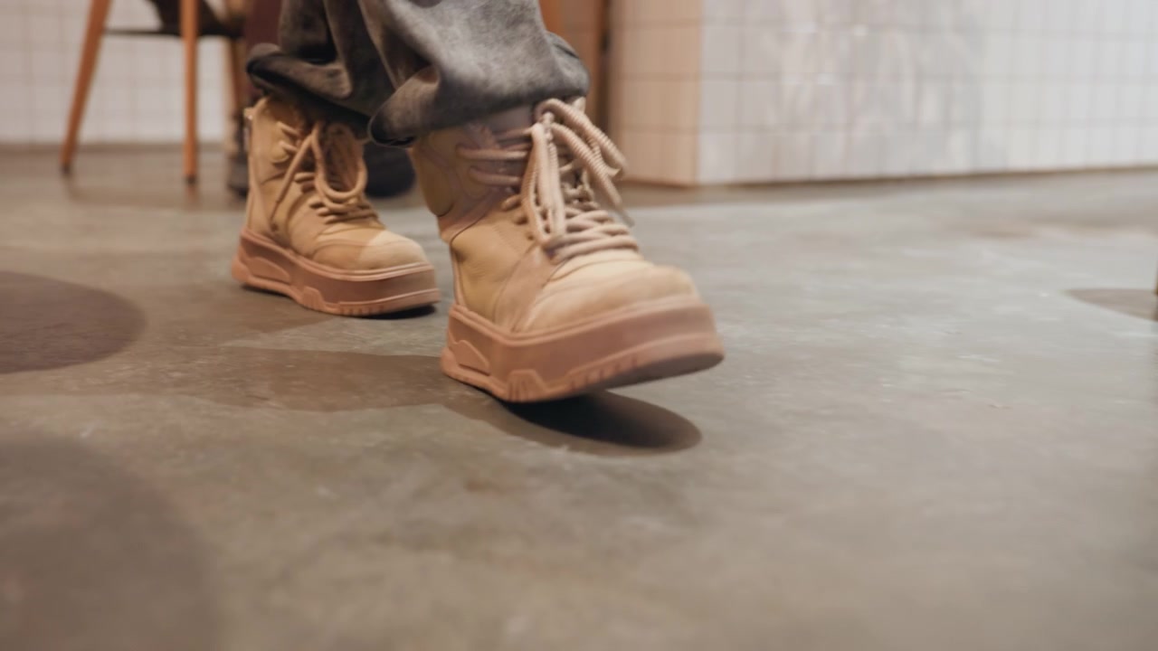 コンクリートの床でベージュのブーツを履き、足を叩く人。