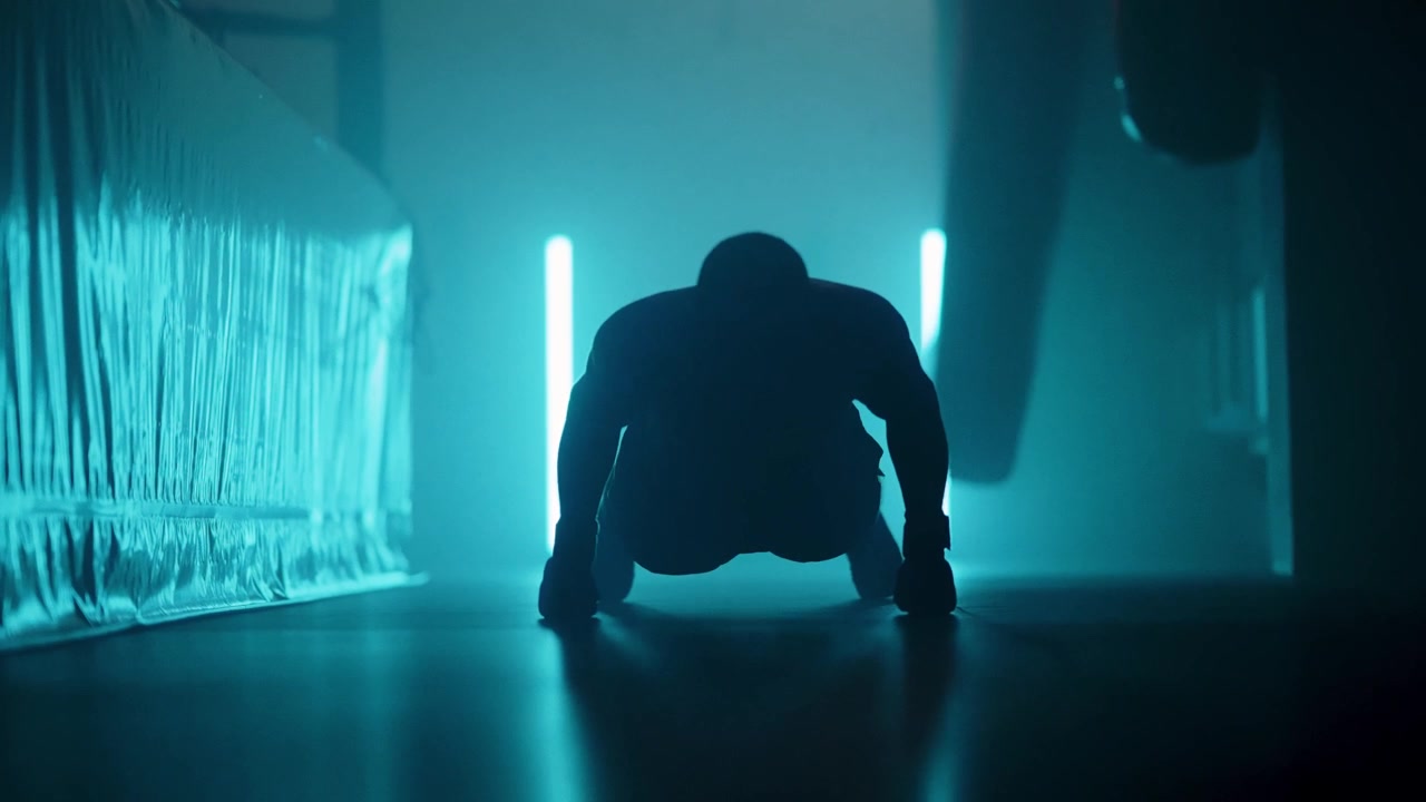 Man doing push-ups in silhouette against neon blue lights