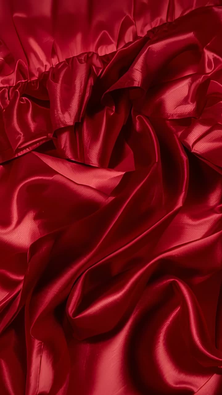 Vídeo vertical: luz cambiante que mueve un satén rojo, resaltando los pliegues brillantes y la costura fruncida en la cama