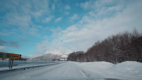 POV-footage-of-a-winter-drive,-showcasing-snowy-mountain-roads-and-the-stunning-view-of-fjords-under-a-clear-blue-sky