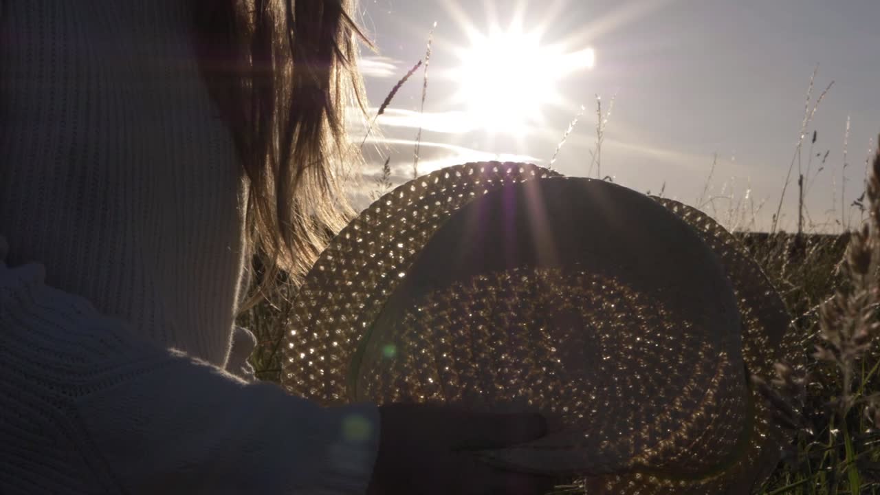 Woman using straw hat as a fan at sunset silhouette close up shot