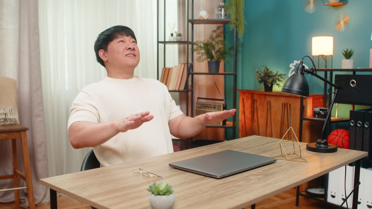 Asian man ending workday removing glasses and closing laptop leaning back happy by completed goals