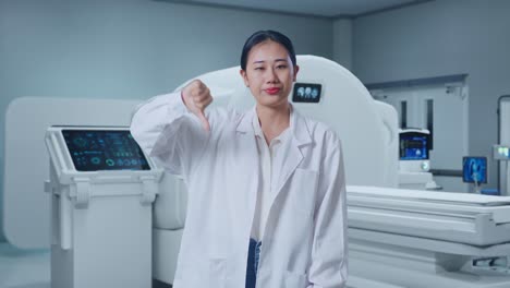 asian woman doctor showing thumbs down gesture while standing with mri machine in the hospital