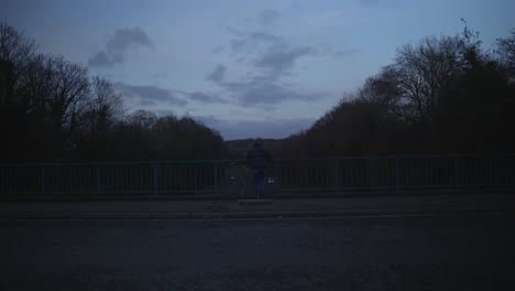 skater leans up against guardrail in silhouette at dusk by river edge with ambient reflections, moody vibe