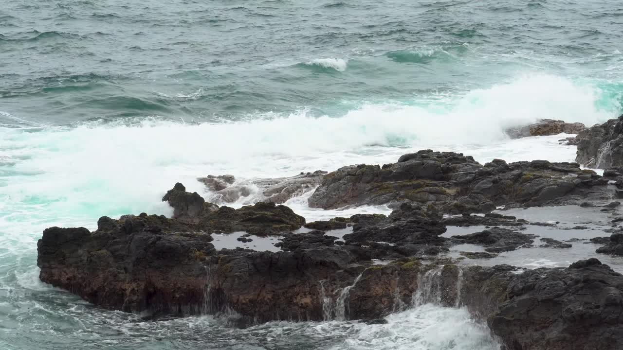 las olas ásperas chocan contra las rocas irregulares cerca del baño de la reina, kauai, hawai