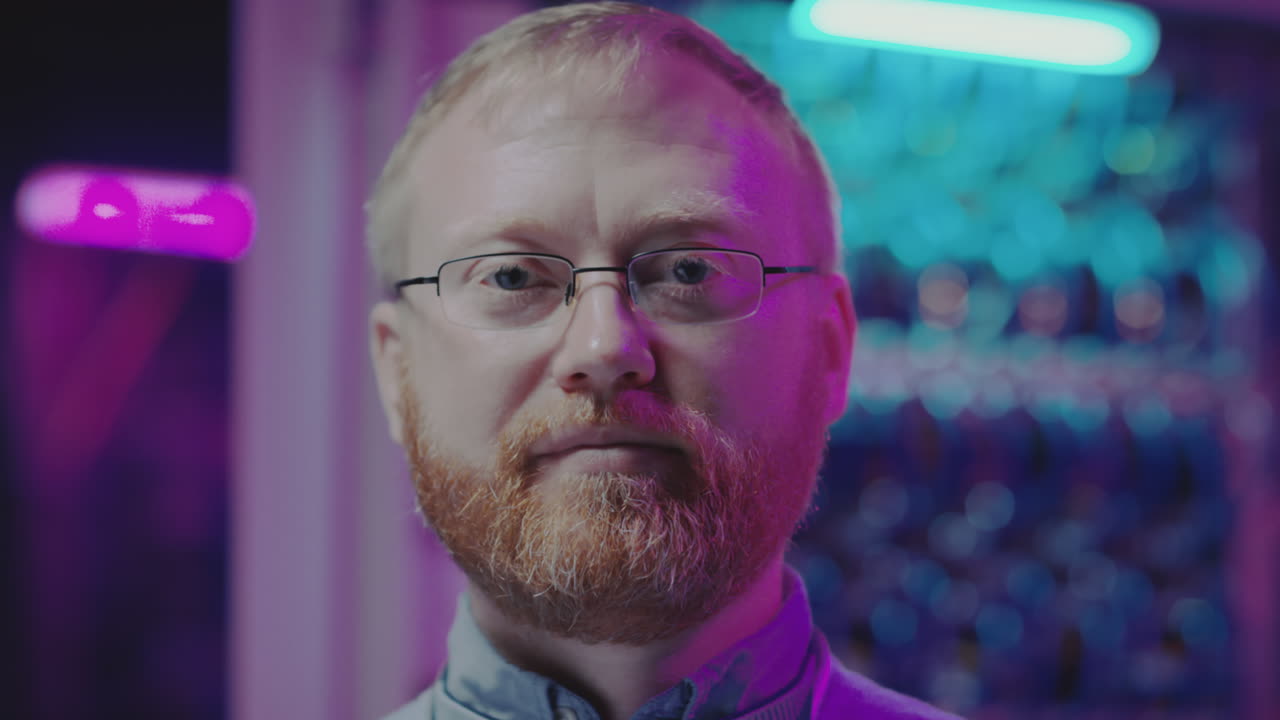 Close-up portrait of a man with a beard and glasses against a backdrop of colorful, blurred lights