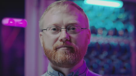 close-up portrait of a man with a beard and glasses against a backdrop of colorful, blurred lights