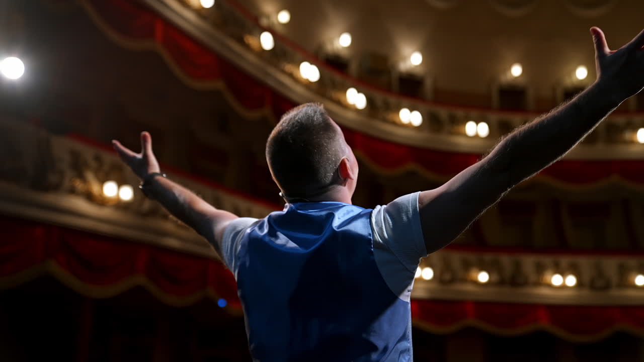 Man rehearses on stage. Actor performing from the scene gesticulating a lot on modern theater background. Rear view.