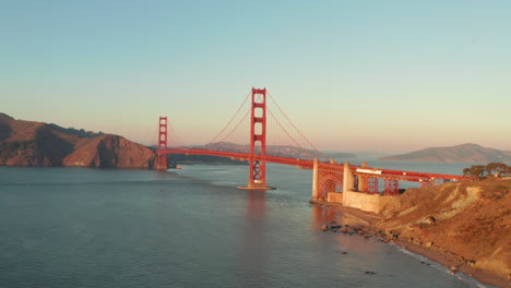 wide circling aerial shot around the golden gate bridge glowing in the sunset