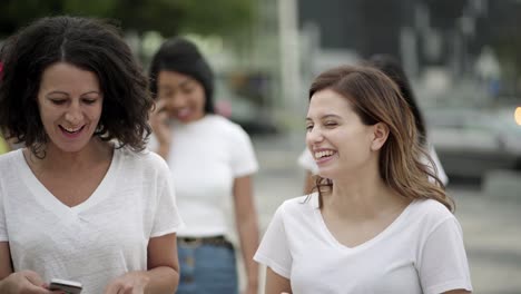 cheerful friends walking on street with phones and talking