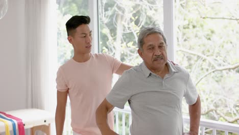 diverse male physiotherapist advising and senior male patient stretching, in slow motion