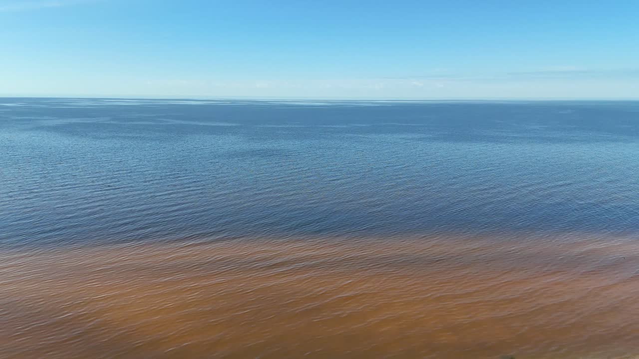 Aerial view of the Baltic Sea in Tūja, Latvia, showing contrast between brown coastal water and deep blue sea, a natural effect from organic coastal runoff and wave patterns