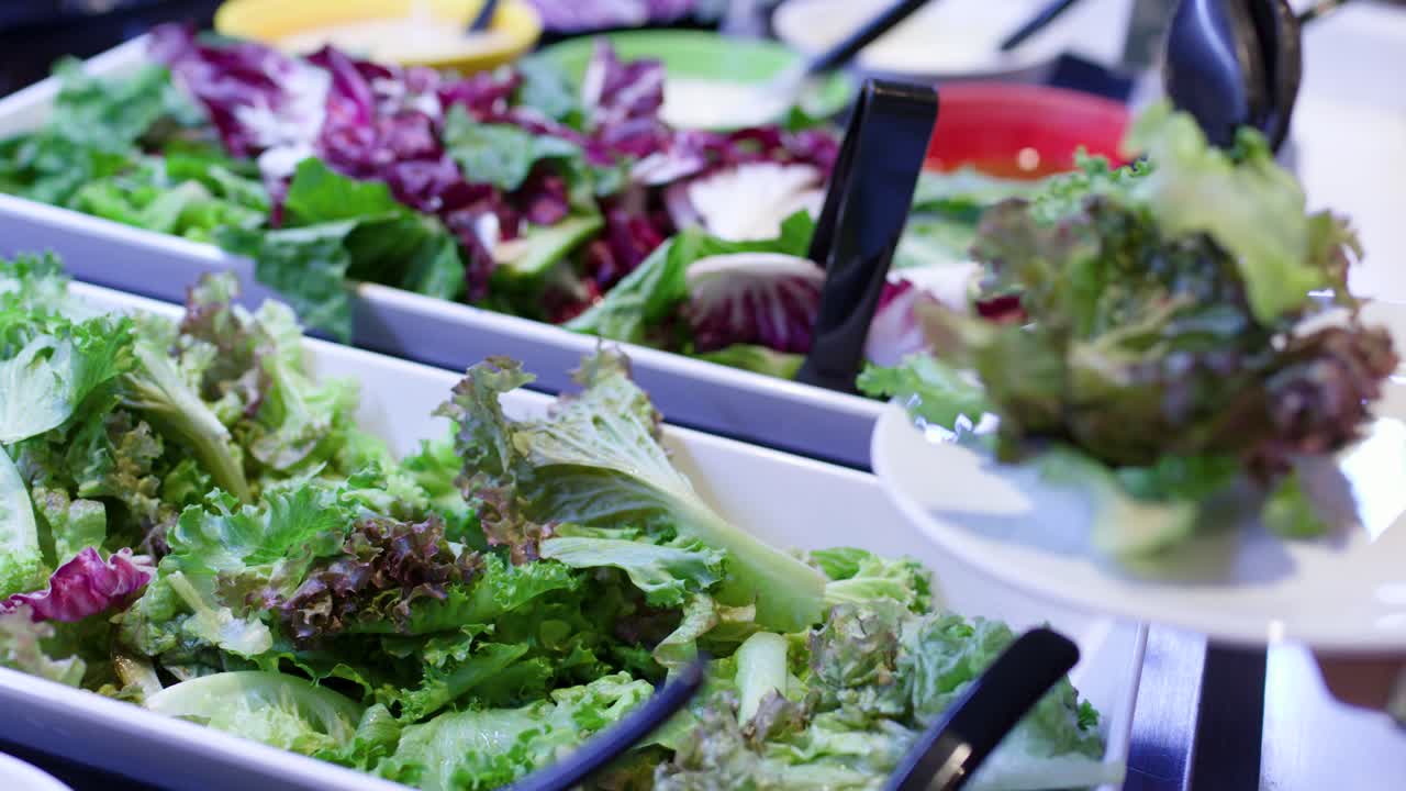 Primo piano di una persona che usa le pinze per servire un'insalata di verdure fresche in un buffet bar luminoso