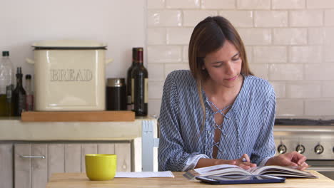 Mujer-Leyendo-Y-Tomando-Notas-En-La-Mesa-De-La-Cocina,-Encerrada,-Filmada-En-R3d