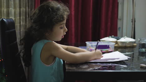 young girl with curly brown hair doing homework seated at a table