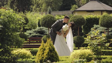 Newlyweds,-caucasian-groom-with-bride-walking,-embracing,-hugs-making-a-kiss-in-park,-wedding-couple