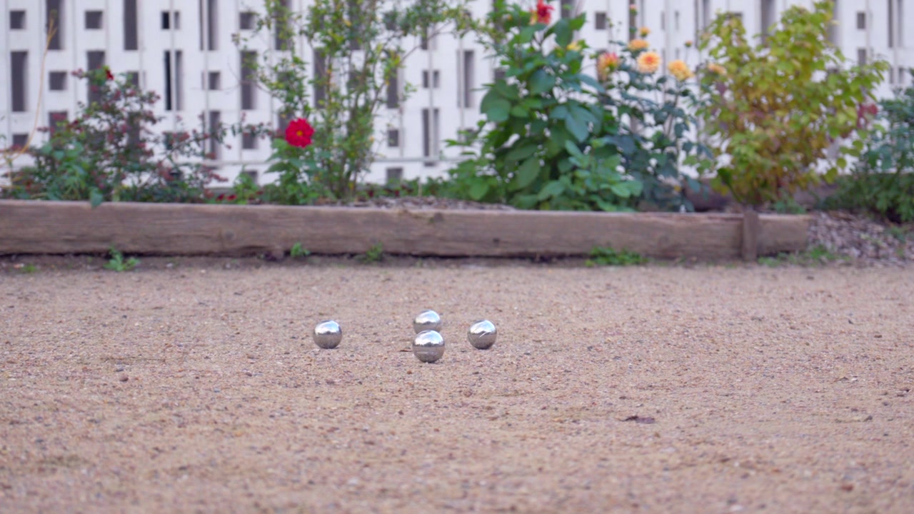 A pétanque ball is thrown but rolls too far from the target.