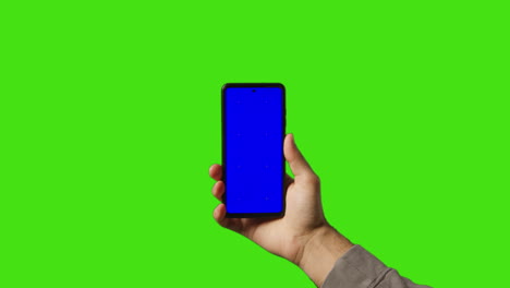 Nahaufnahme-Eines-Mannes,-Der-Ein-Mobiltelefon-Mit-Blauem-Bildschirm-Vor-Einem-Grünen-Hintergrund-Hält