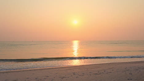 Mientras-Las-Olas-Golpean-Una-Tranquila-Playa-De-Arena,-Las-Puestas-De-Sol-En-El-Horizonte