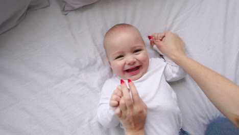 baby in white t-shirt lying on a white bed and laughing looking at the camera top view slow motion