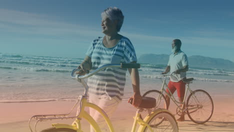 spots of light against african american senior couple with bicycles walking together at the beach