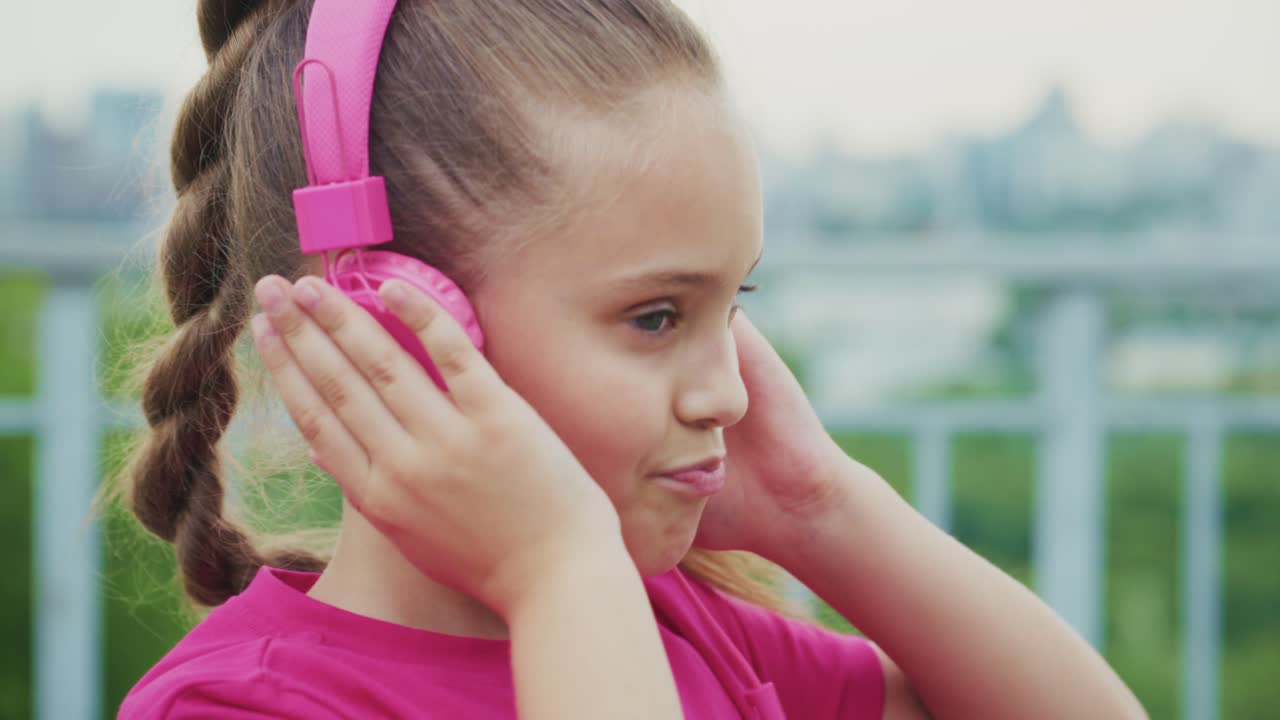 A Young Girl Enjoying Music with Pink Headphones: Capturing the Joy of Listening in a Serene Urban Environment