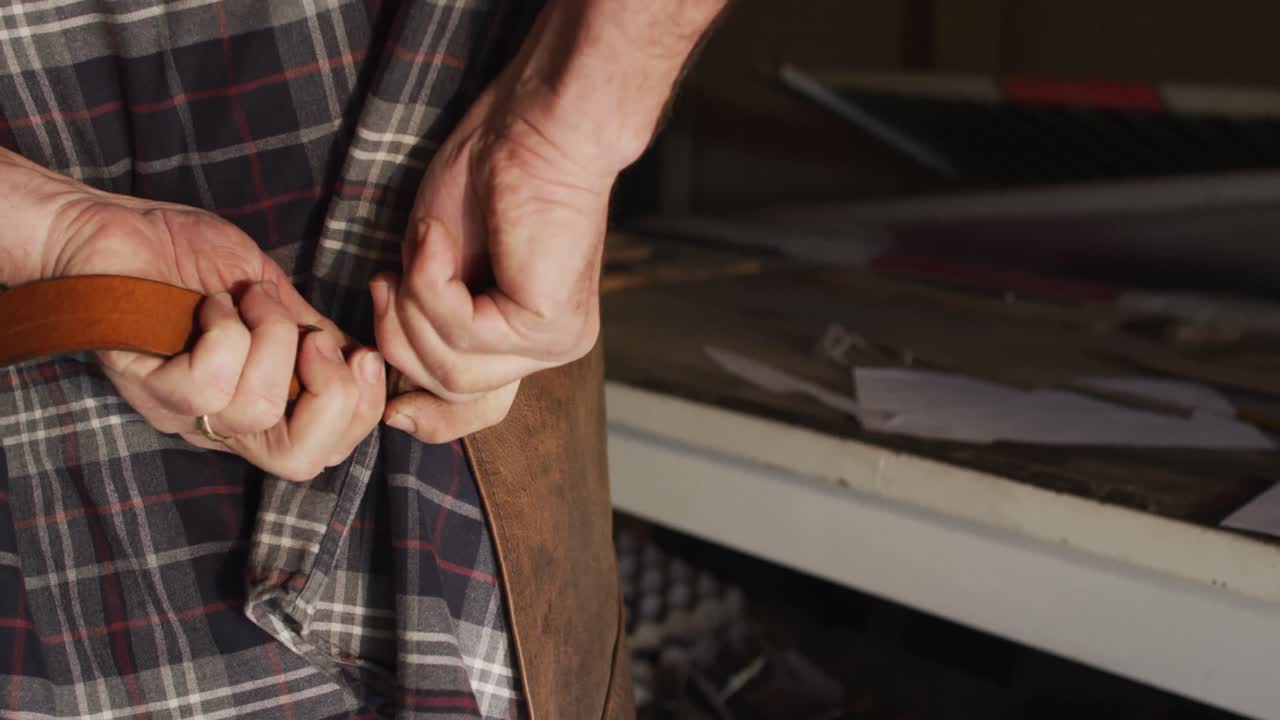 cerca de las manos de un hombre caucásico fabricante de cuchillos en un taller atando un delantal
