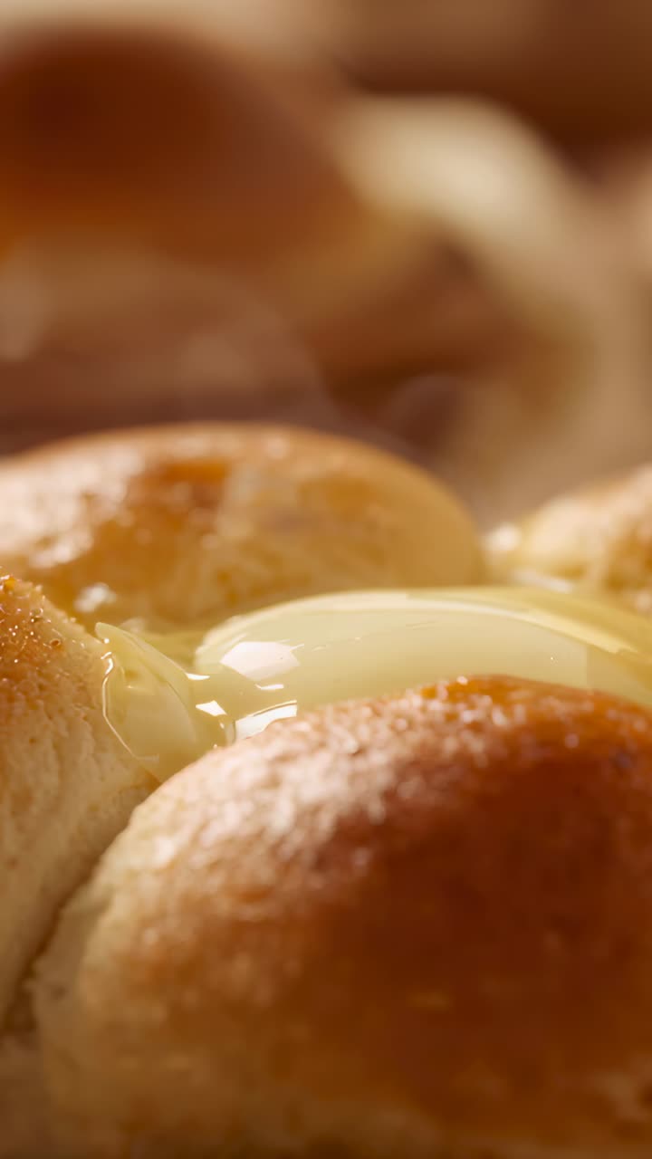 Vertical video: Landing butter pat melting across warm roll cluster on tray, with blurred braid