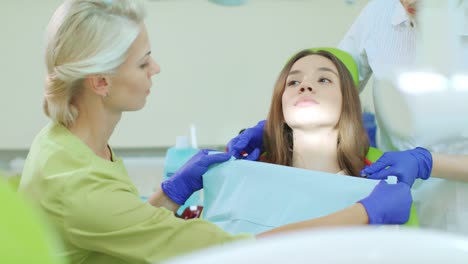 Dentist-with-assistant-preparing-for-dental-treatment.-Patient-in-dentist-chair