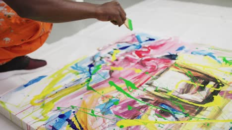 Close-up-of-african-american-male-artist-pouring-paint-with-a-paint-brush-on-canvas-at-art-studio