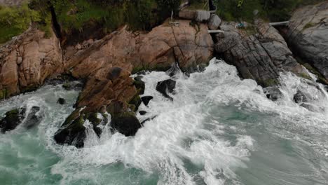 acercándose a la vista aérea de las olas del océano rodando al golpear las rocas del acantilado de la playa de joatinga en río de janeiro