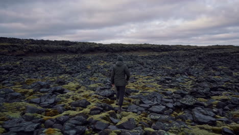 person walking through a moss-covered lava field under a cloudy sky