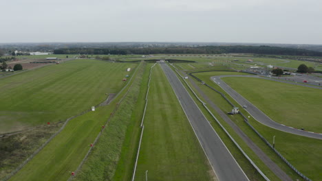 Cars-racing-round-a-track-surrounded-by-green-fields-with-grey-skies