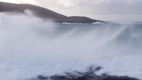 Slow-motion,-panning-shot-of-a-large-wave-crashing-over-the-rocks-during-a-storm-in-the-sea-by-Tangasdale-beach,-near-Castlebay-on-the-Isle-of-Barra