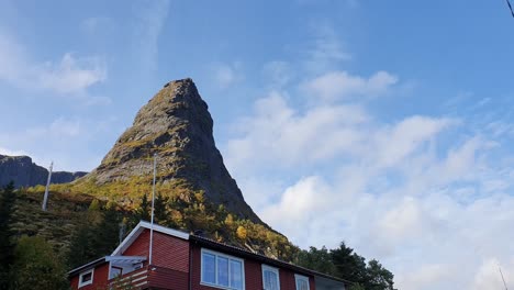 view over a red norwegian hut at the foot of a tippy mountain against a blue sky