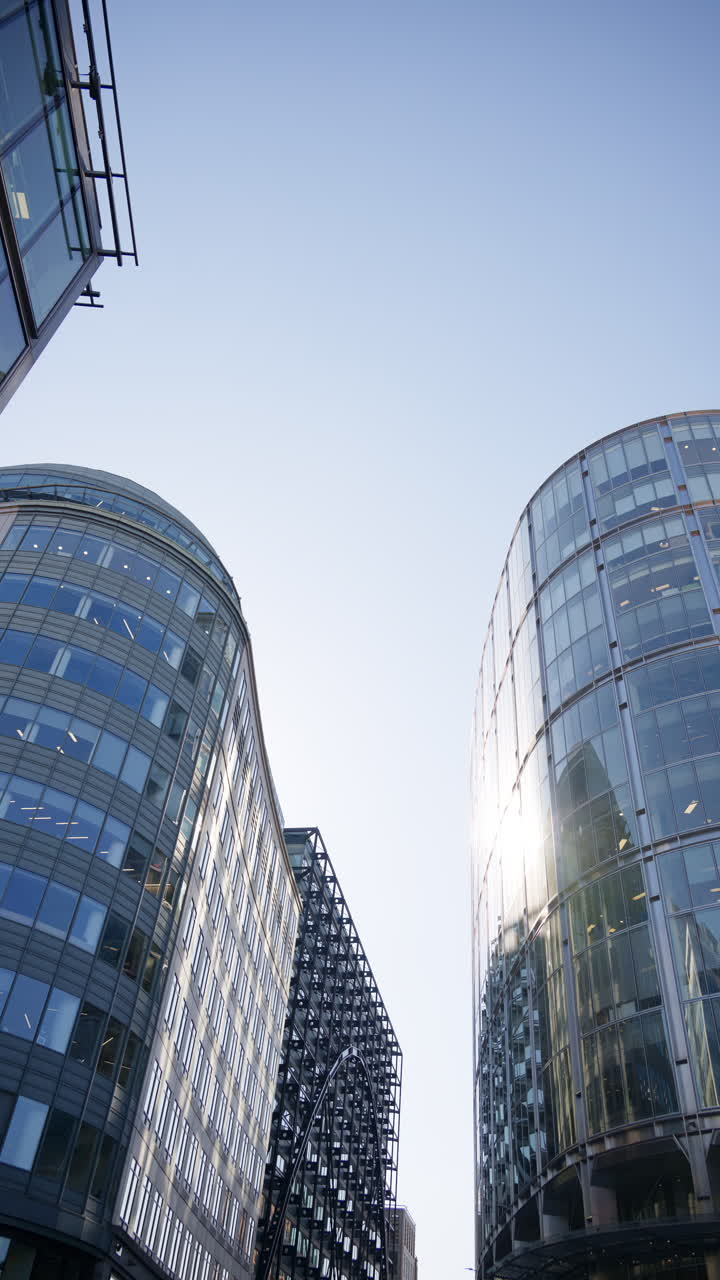 Modern glass skyscrapers of London's financial district reflecting the blue sky next to historic architecture. Vertical