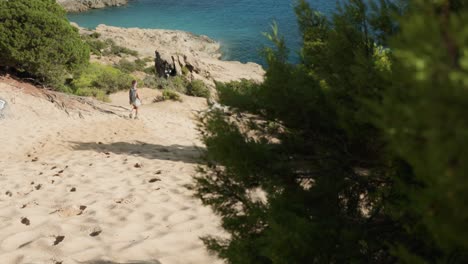 slow motion footage of a solo woman backpacker walks freely across the golden sand dunes at las salinas beach in ibiza, spain, during a bright sunny day.