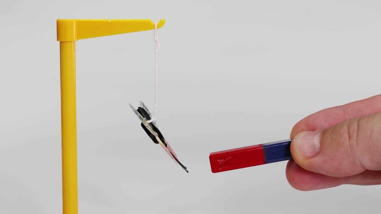 A magnet influences a suspended butterfly model, demonstrating magnetic attraction and repulsion in a controlled environment
