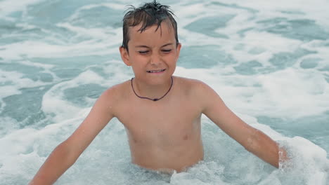 cheerful man swashing in sea surf. happy teenager wiping face at seaside.