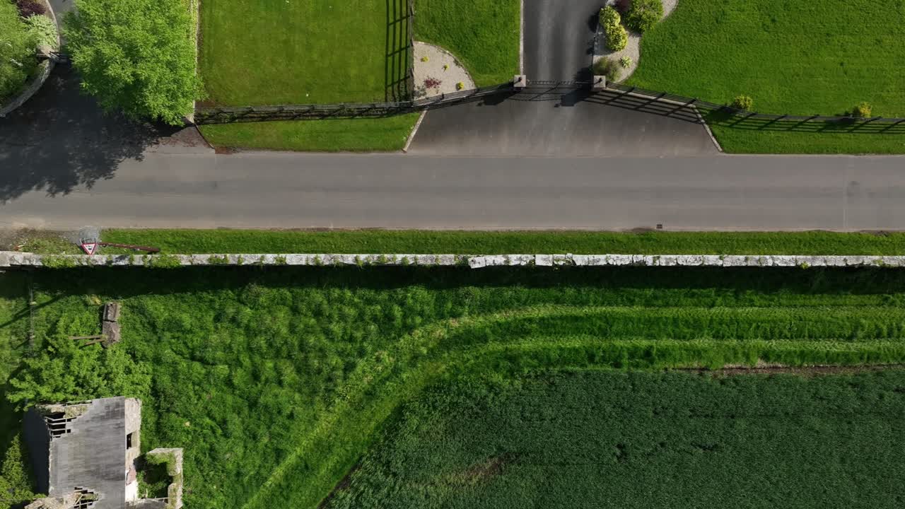Caledon Border Wall, County Tyrone, Northern Ireland, May 2023. Drone birdseye aerial view moving right over stone heritage, road with passing car and abandoned stone cottage.