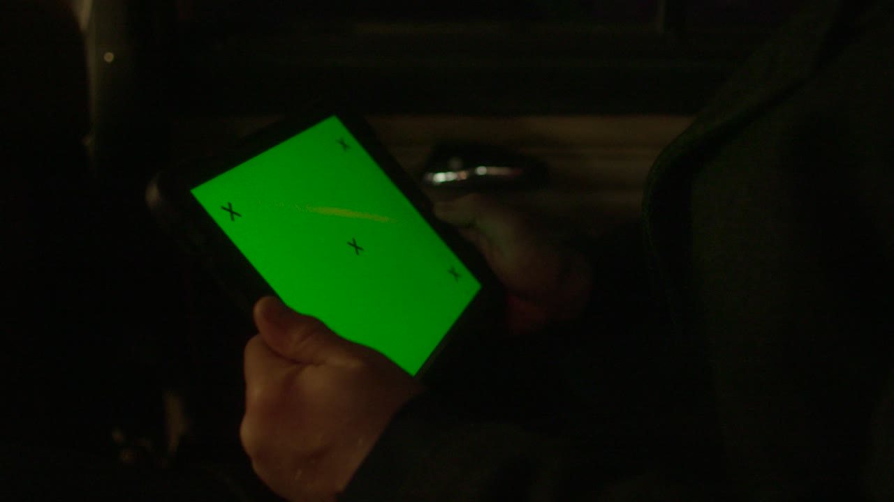 밤에 차에서 녹색 화면을 가진 태블릿을 사용하는 사람