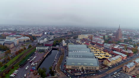 Luftrückwärtsflug-über-Die-Stadt-Riga-Mit-Markthalle-An-Bewölkten-Tagen,-Lettland