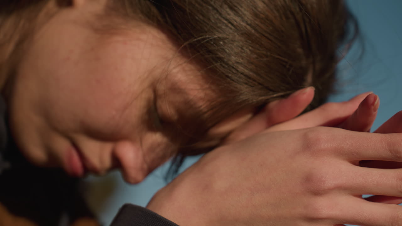 Close-up shot of hands gently rubbing together, gesture of deep contemplation and grief. The head is partially visible, suggesting a moment of sorrow and reflection against a clear sky backdrop