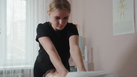 massage therapist pressing hands on client s back during session in softly lit room with anatomy chart on pink wall, light curtain-covered window, and wellness tools enhancing therapeutic environment
